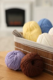 Photo of Colorful yarns and basket on wooden table indoors, closeup