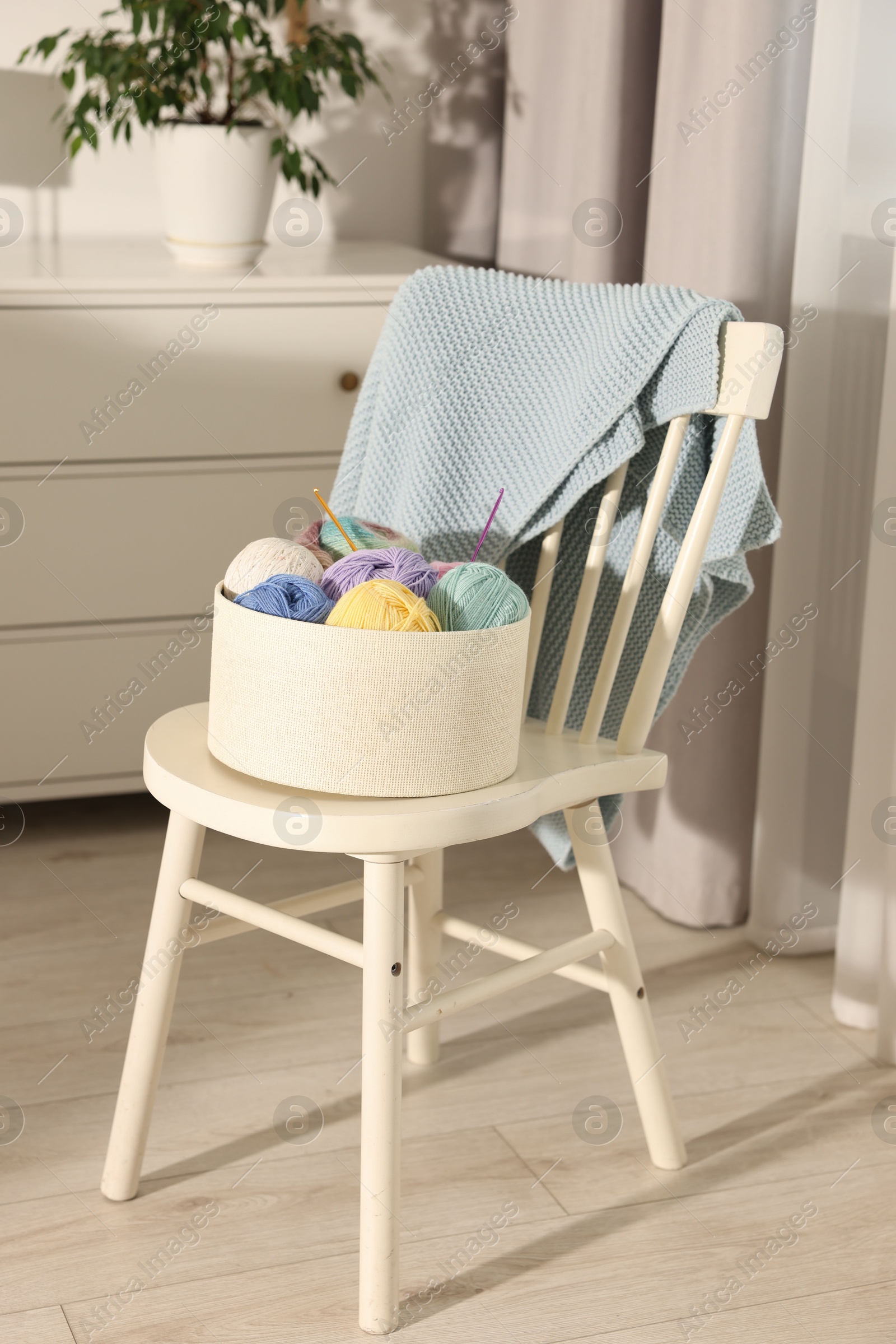 Photo of Box with colorful yarns and crochet hooks on chair indoors