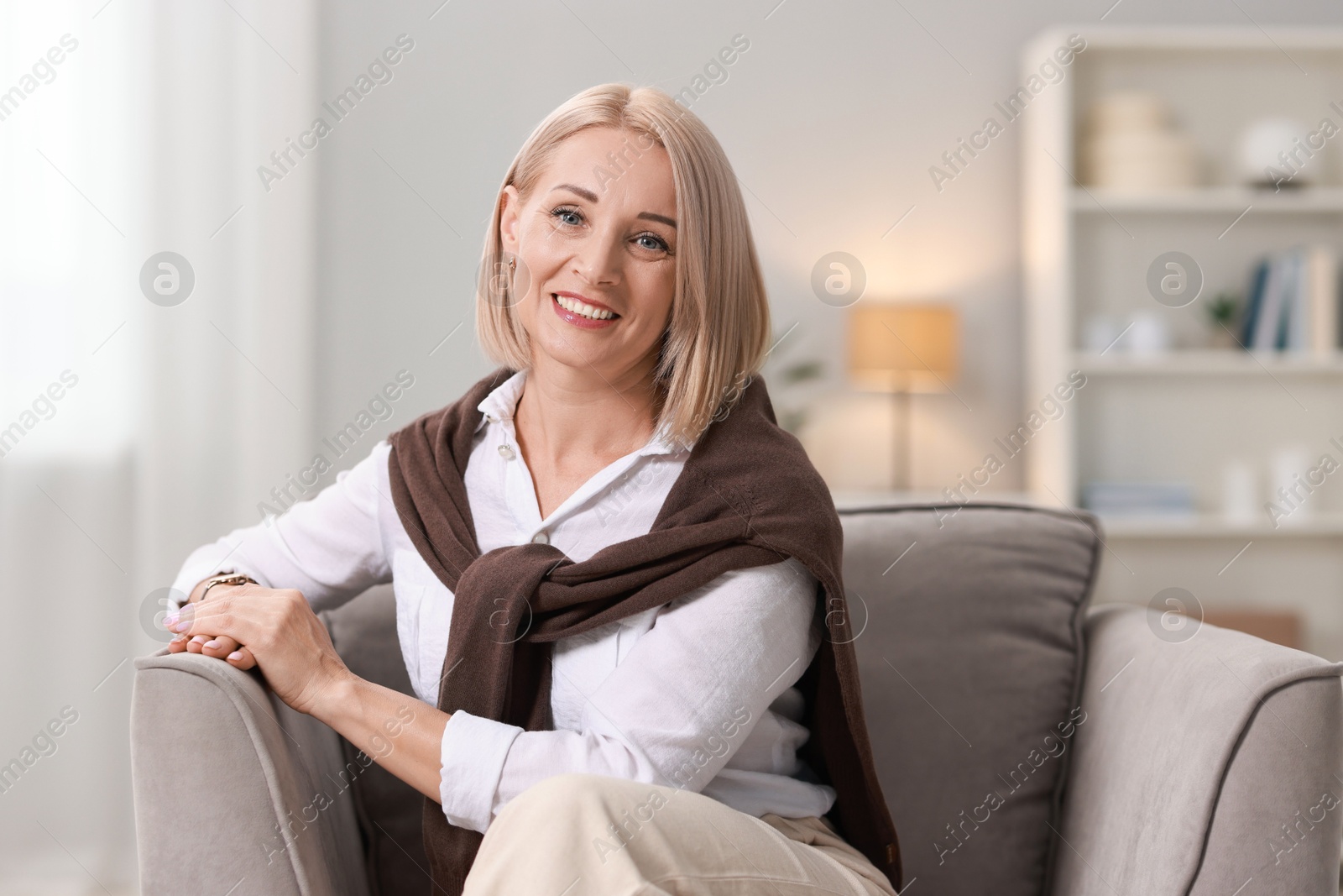 Photo of Portrait of smiling middle aged woman sitting on armchair at home