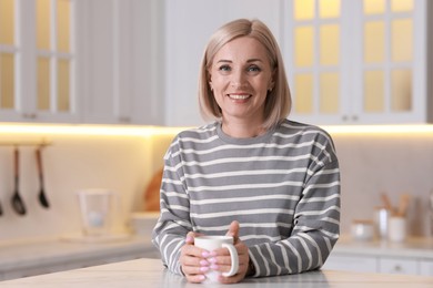 Smiling middle aged woman with cup of hot drink in kitchen