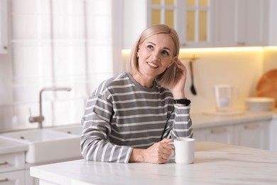 Photo of Smiling middle aged woman with cup of hot drink in kitchen