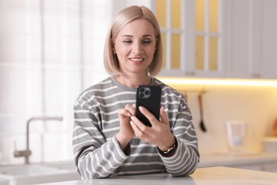 Portrait of smiling middle aged woman using smartphone in kitchen