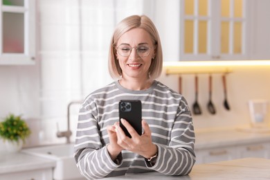 Photo of Portrait of smiling middle aged woman using smartphone in kitchen