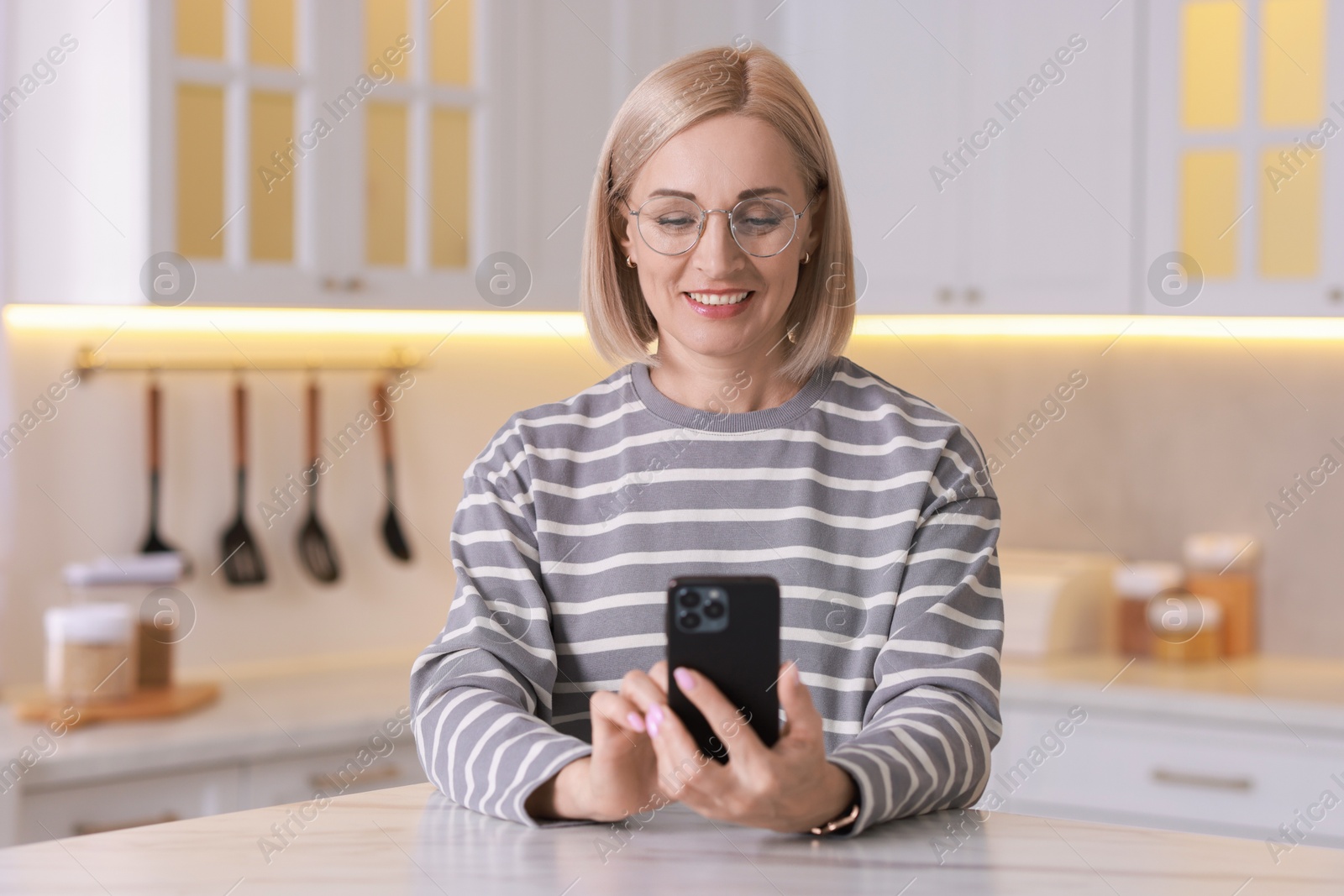 Photo of Portrait of smiling middle aged woman using smartphone in kitchen