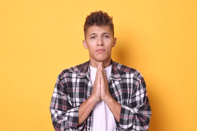 Photo of Young student praying for good exam result on yellow background