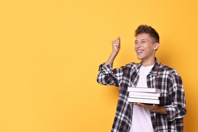 Photo of Young student with stack of books happy about his good exam result on yellow background, space for text