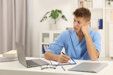 Medical student taking notes while studying at table indoors