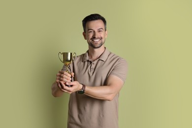 Photo of Happy winner with golden trophy cup on pale olive background