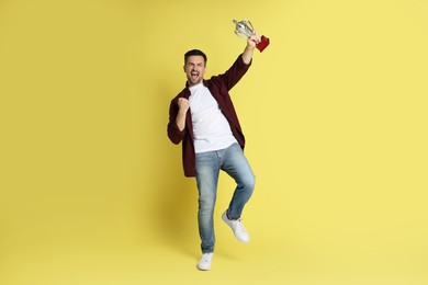 Photo of Happy winner with golden trophy cup on yellow background