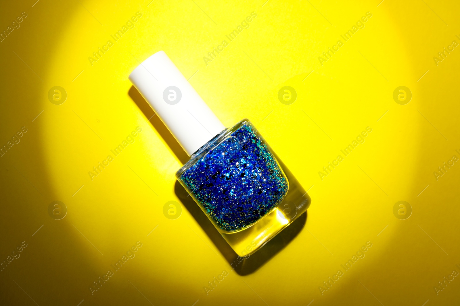 Photo of Nail polish in bottle on yellow background, top view