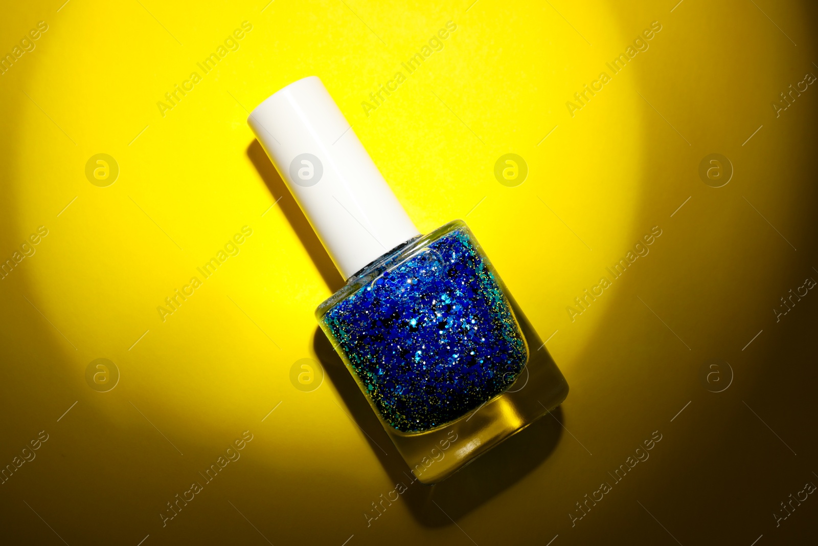 Photo of Nail polish in bottle on yellow background, top view