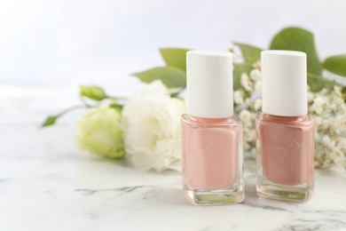 Photo of Nail polishes in bottles on white marble table, closeup. Space for text