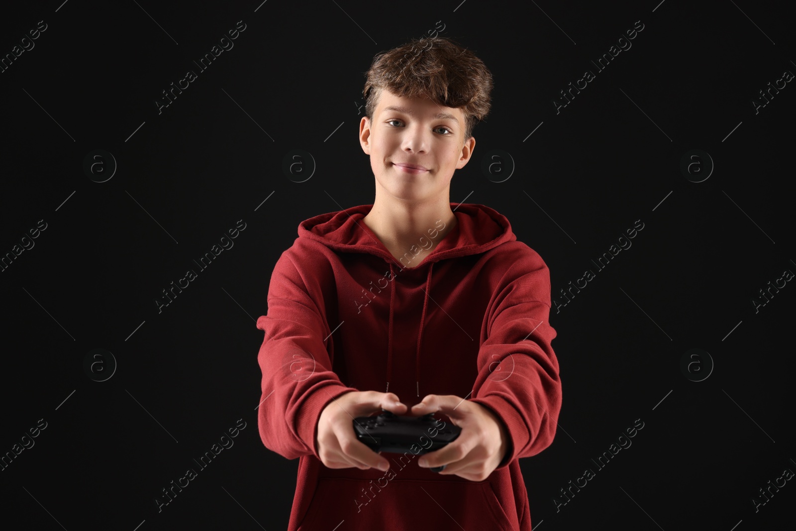 Photo of Teenage boy playing video game with controller on black background