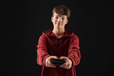 Teenage boy playing video game with controller on black background