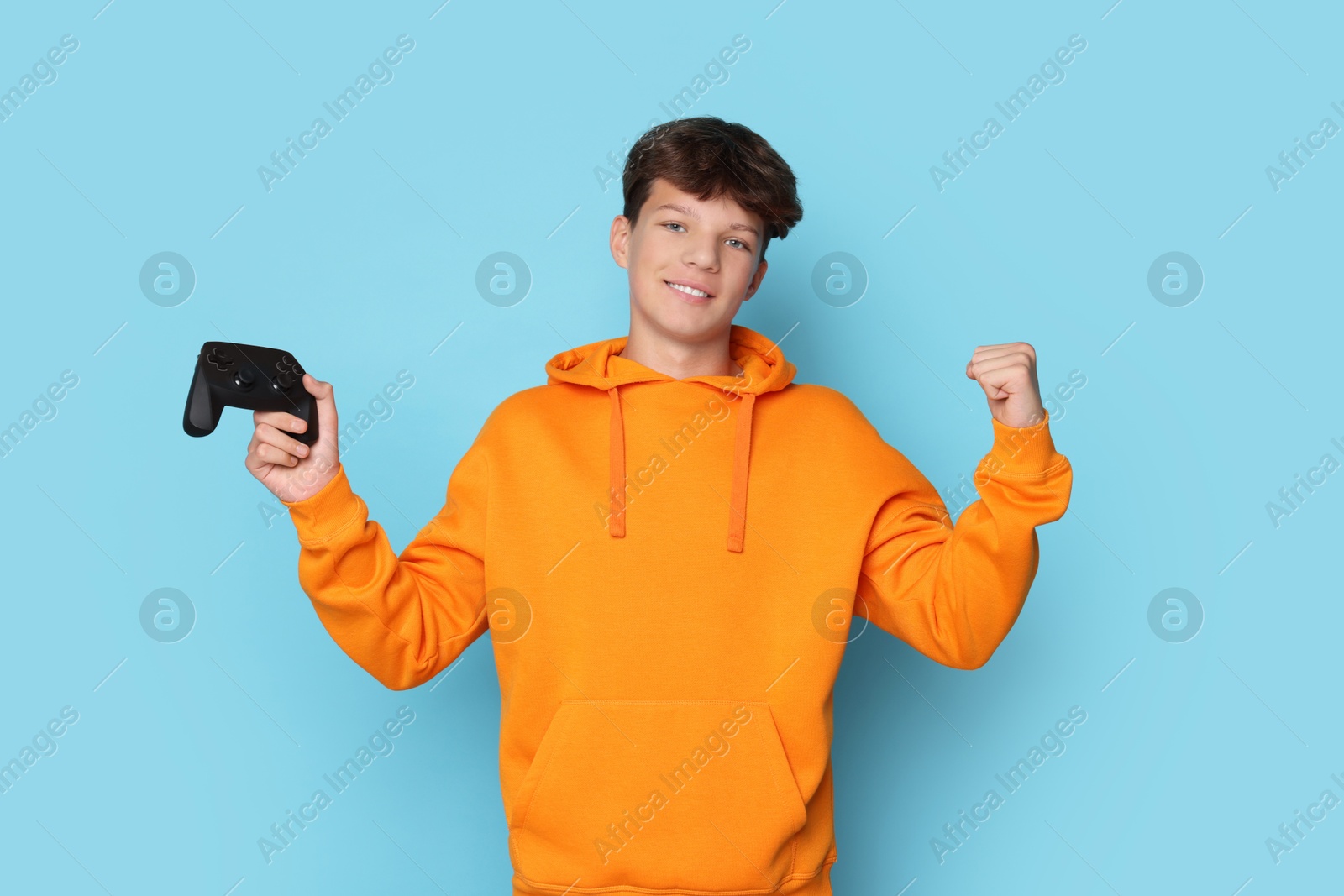 Photo of Happy teenage boy with controller on light blue background