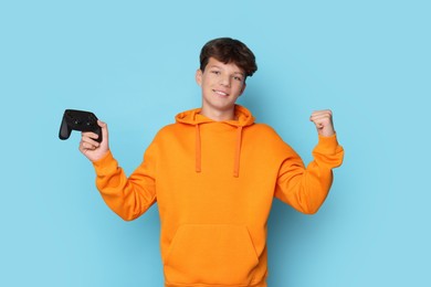 Happy teenage boy with controller on light blue background