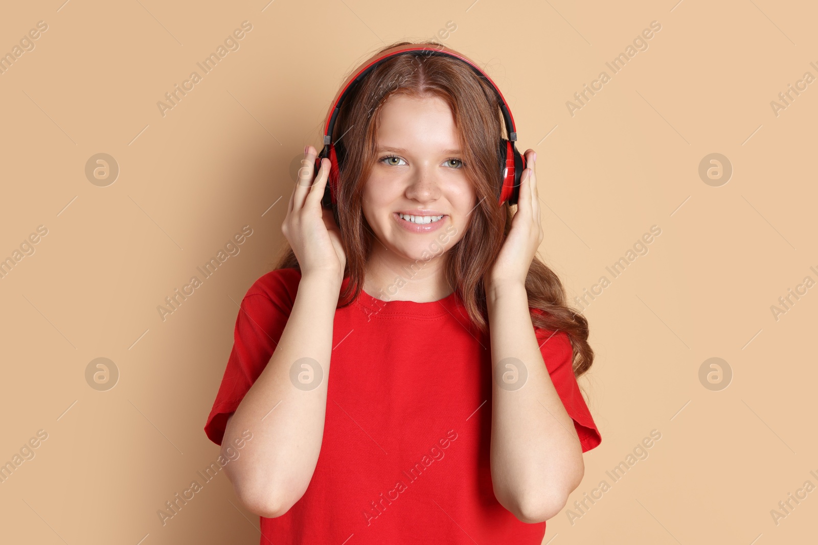 Photo of Smiling teenage girl in headphones listening to music on beige background