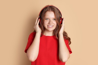 Photo of Smiling teenage girl in headphones listening to music on beige background