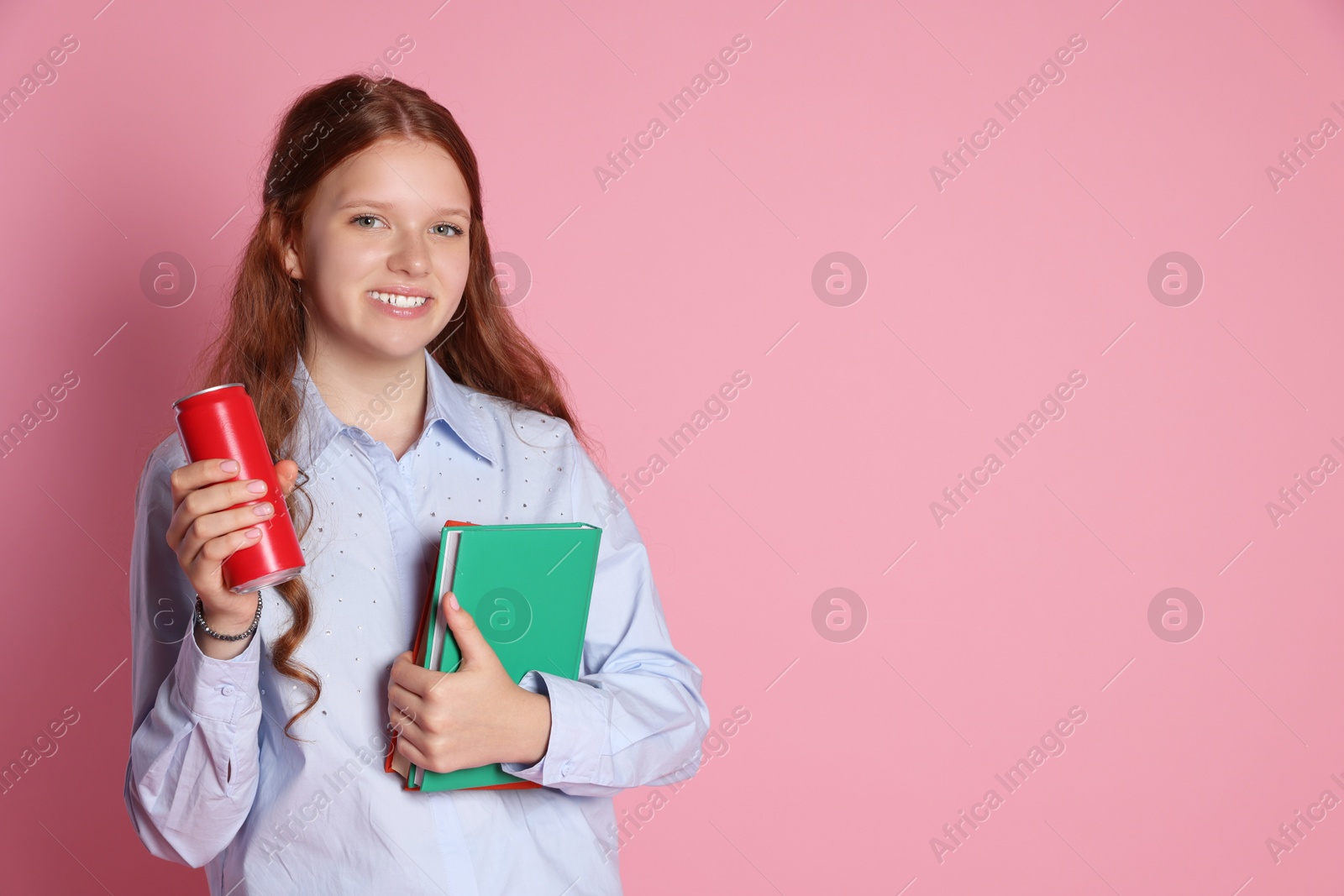 Photo of Smiling teenage girl with books and can on pink background. Space for text