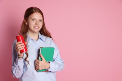 Smiling teenage girl with books and can on pink background. Space for text