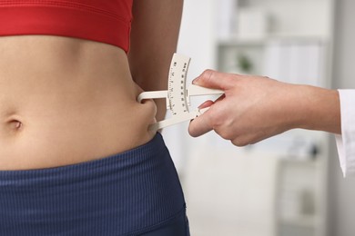 Photo of Doctor measuring woman's body fat with caliper in clinic, closeup