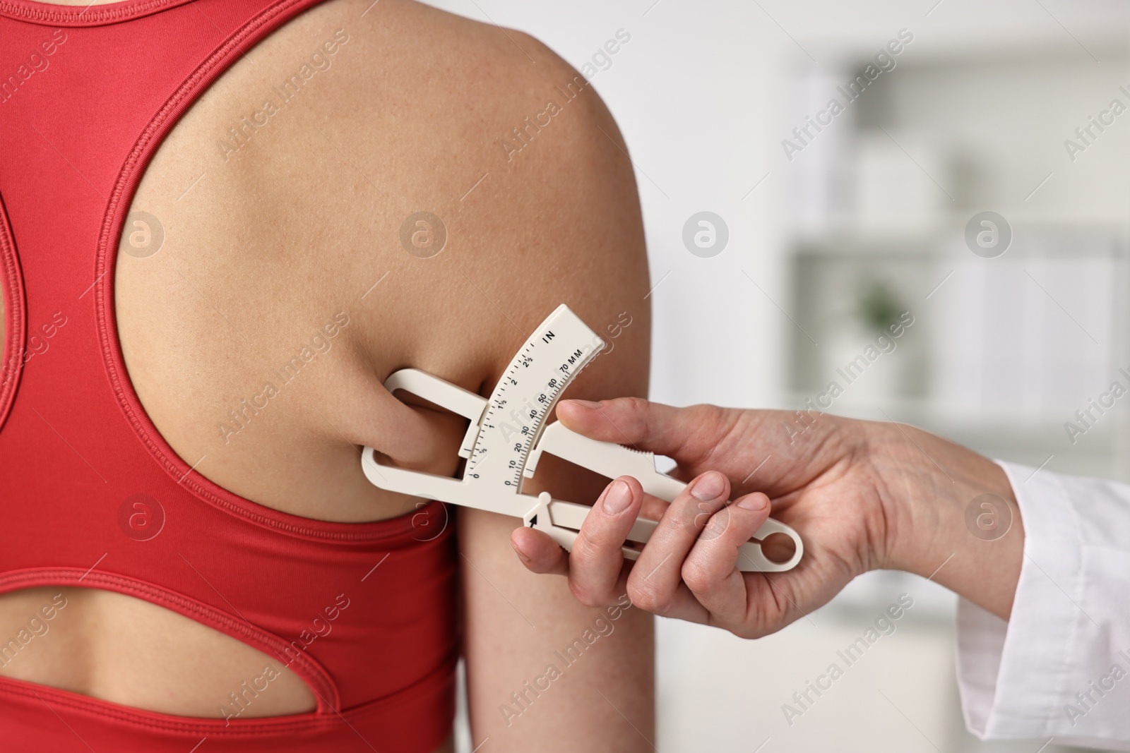 Photo of Doctor measuring woman's body fat with caliper in clinic, closeup