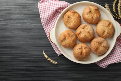 Photo of Baking dish with homemade tasty buns and spikelets on black wooden table, flat lay. Space for text