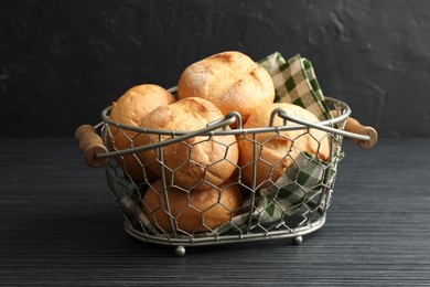 Photo of Metal basket with homemade tasty buns on black wooden table