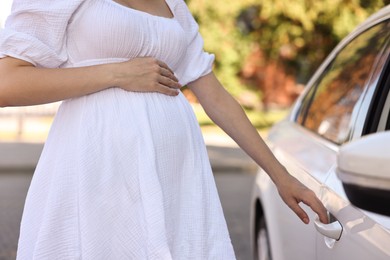 Pregnant woman opening car door outdoors, closeup