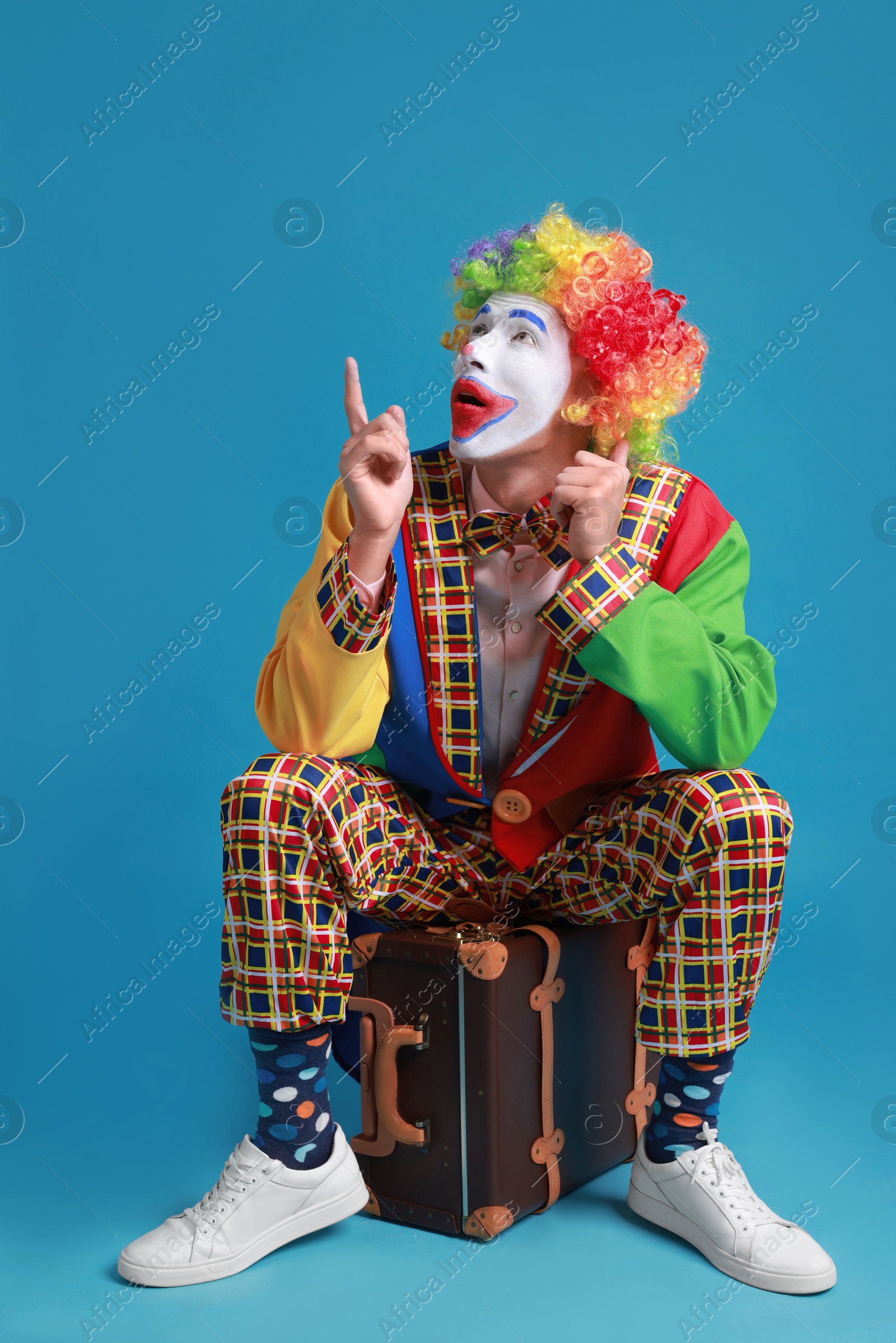 Photo of Clown with suitcase pointing at something on blue background