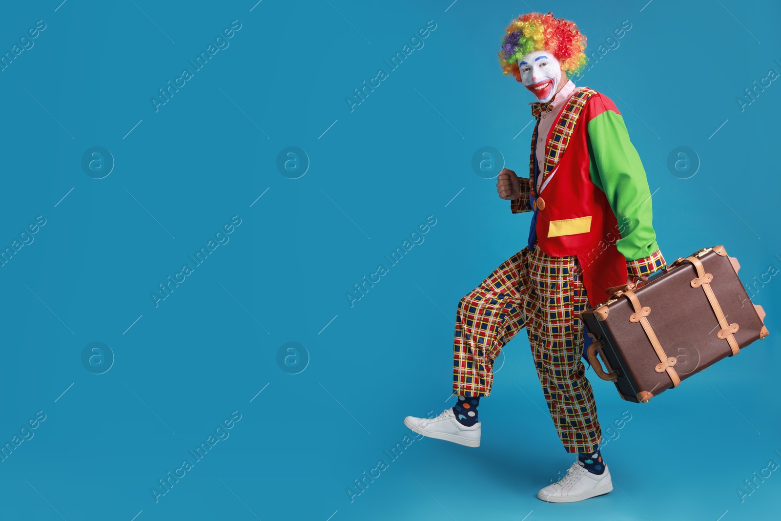 Photo of Funny clown with suitcase on blue background