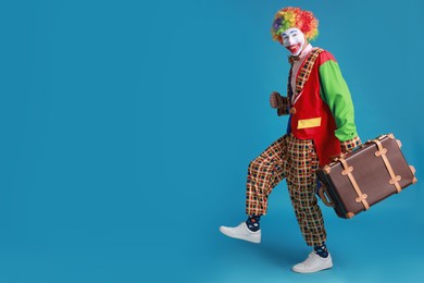 Photo of Funny clown with suitcase on blue background