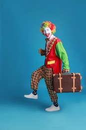 Photo of Funny clown with suitcase on blue background