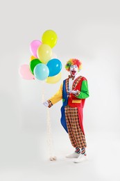 Emotional clown with colorful balloons on light background