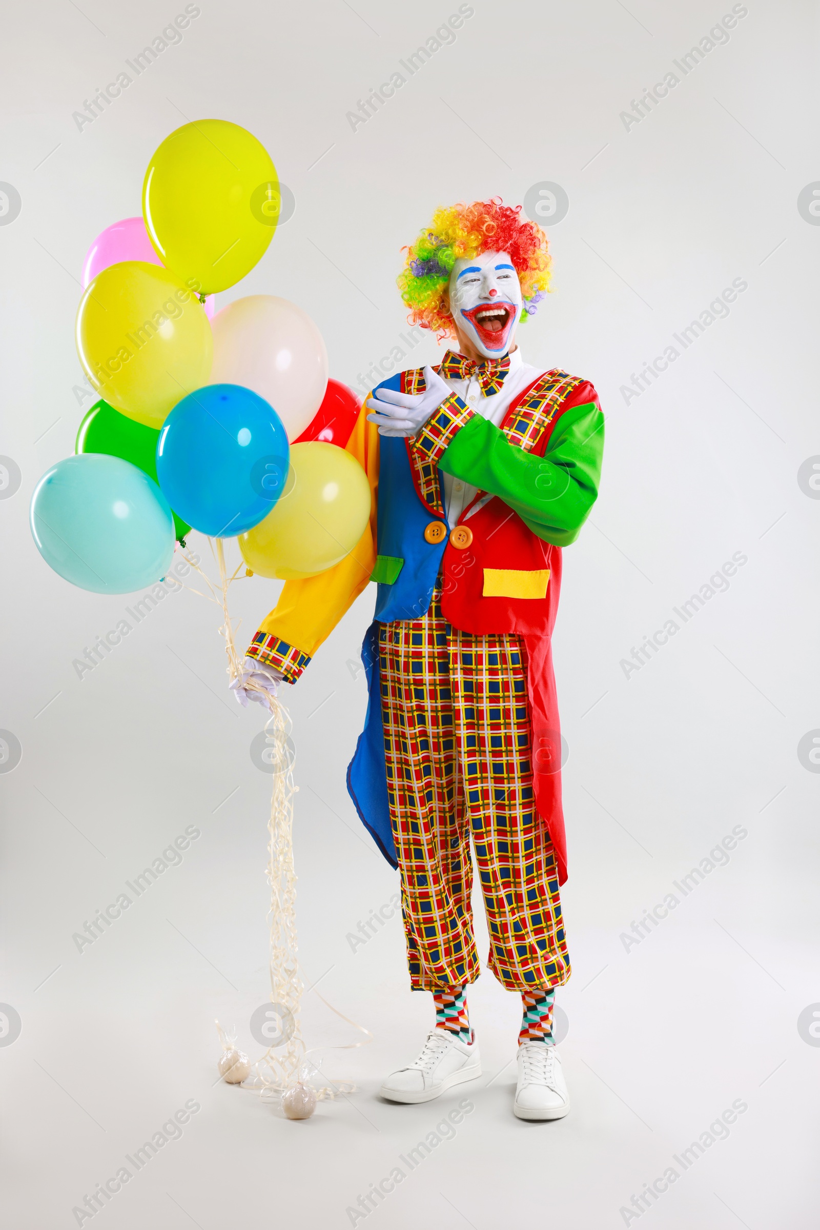 Photo of Happy clown with colorful balloons on light background