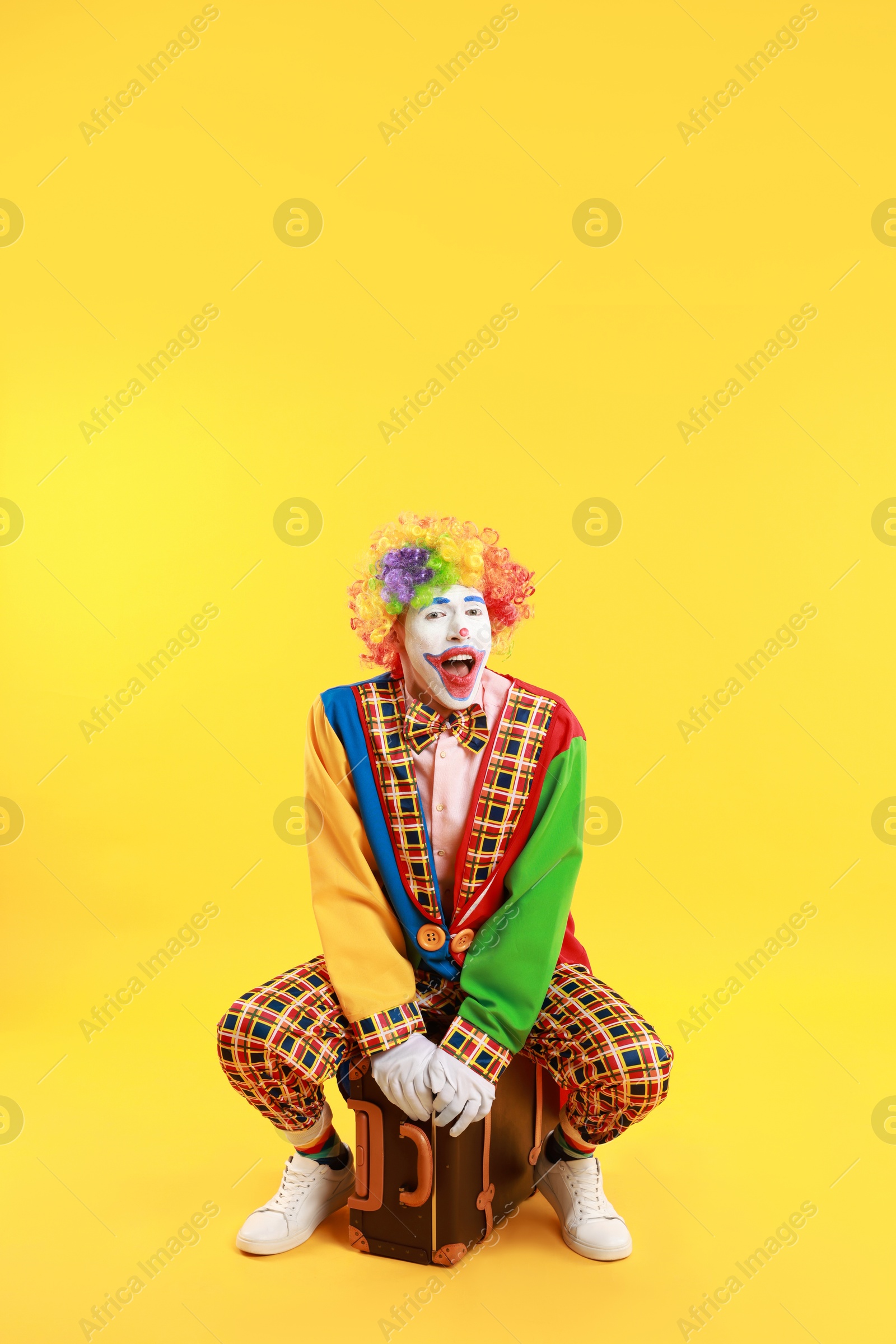 Photo of Emotional clown with suitcase on yellow background