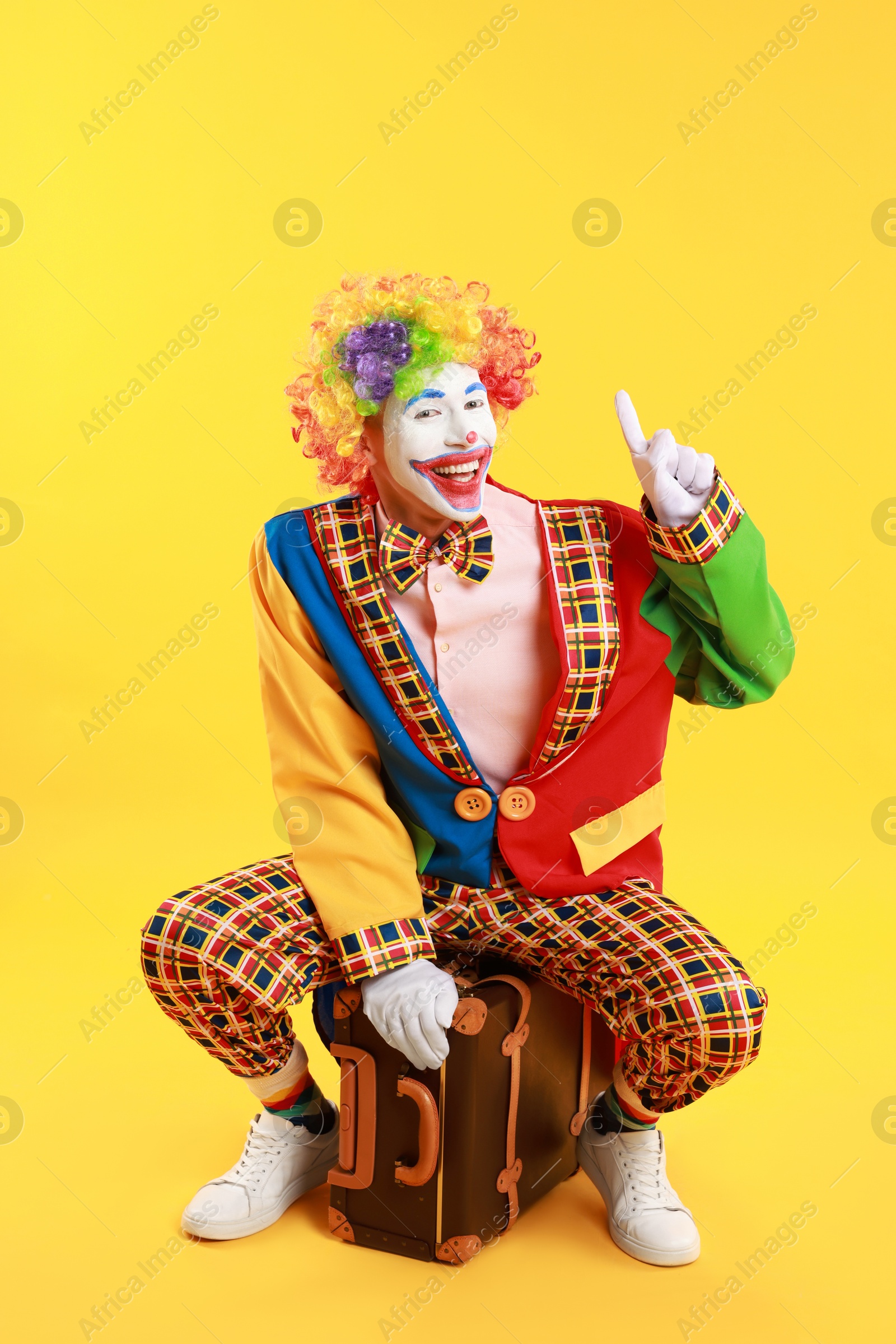 Photo of Happy clown with suitcase on yellow background