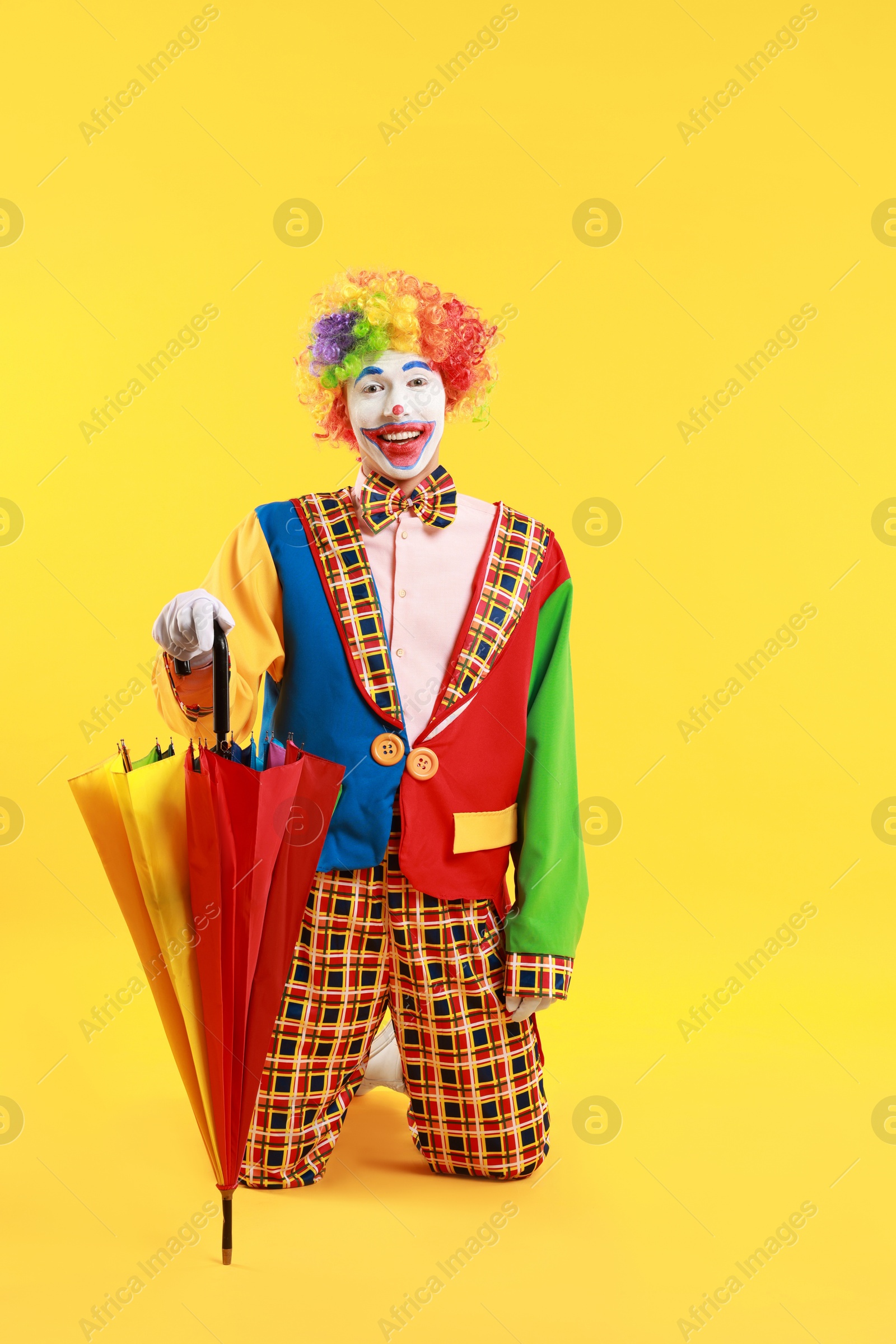 Photo of Happy clown with colorful umbrella on yellow background