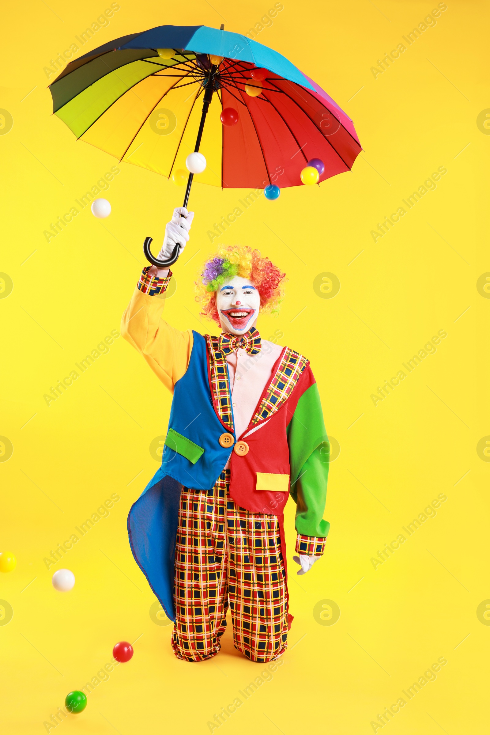 Photo of Happy clown with colorful umbrella on yellow background