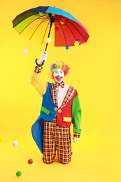 Happy clown with colorful umbrella on yellow background