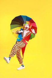 Photo of Emotional clown with colorful umbrella on yellow background