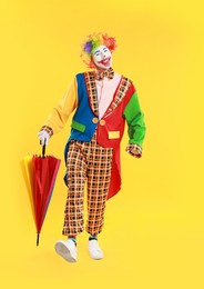 Happy clown with colorful umbrella on yellow background