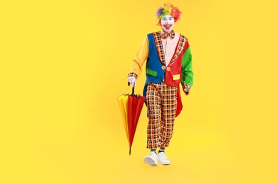 Happy clown with colorful umbrella on yellow background