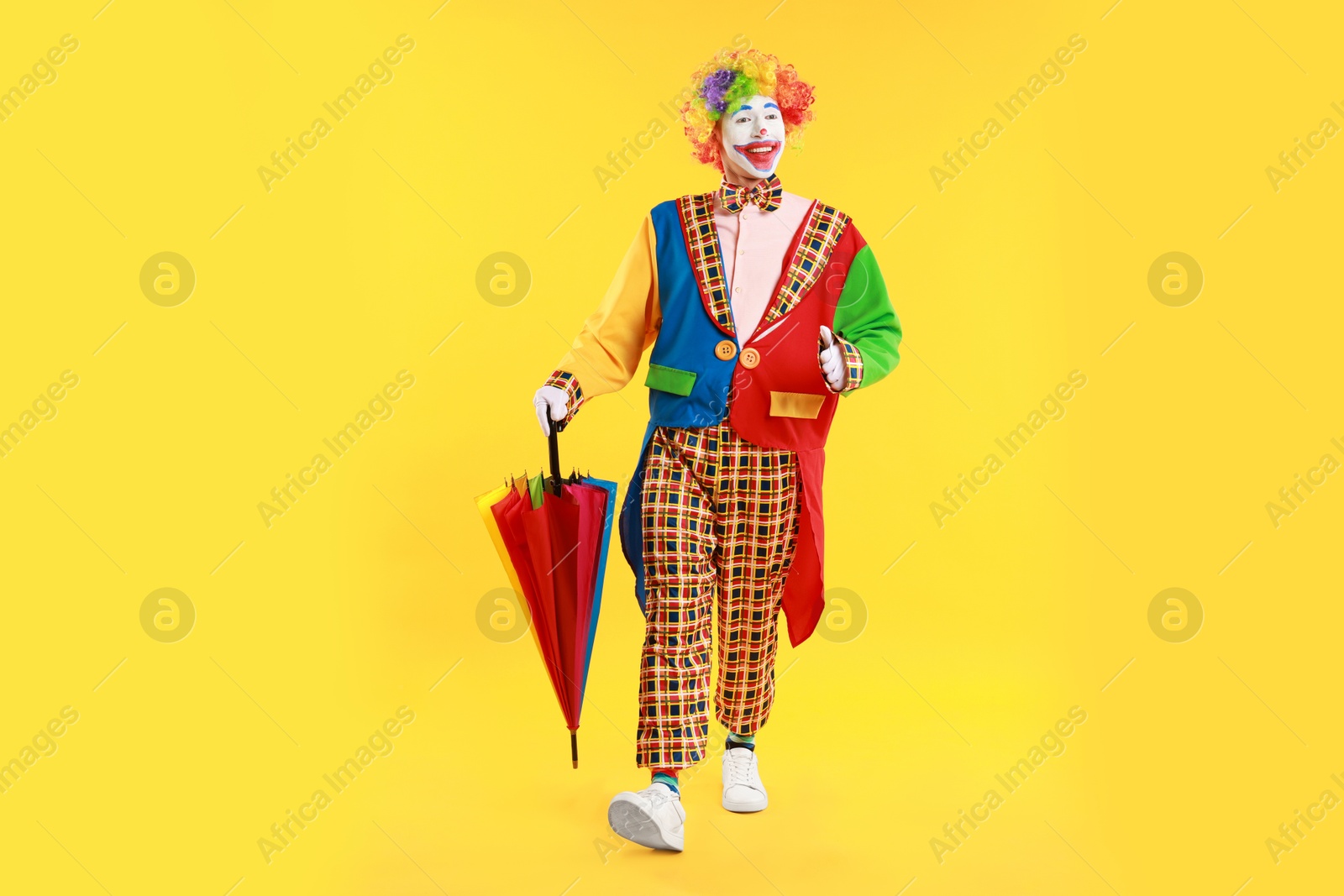 Photo of Happy clown with colorful umbrella on yellow background