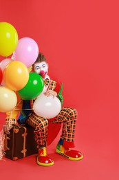 Photo of Clown with colorful balloons and suitcase on red background