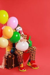 Clown with colorful balloons and suitcase on red background