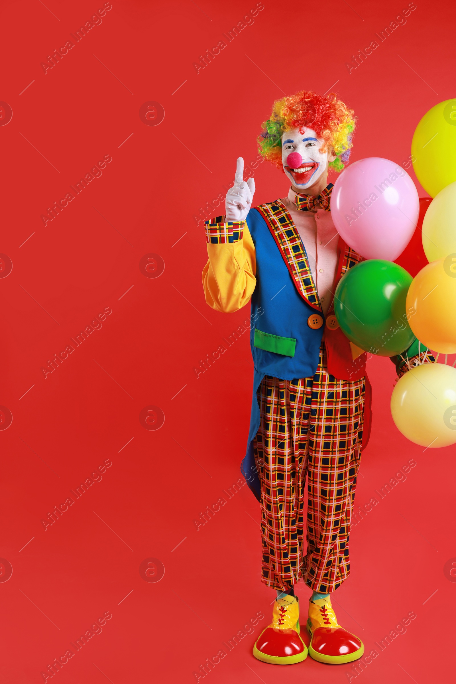 Photo of Happy clown with colorful balloons on red background, space for text