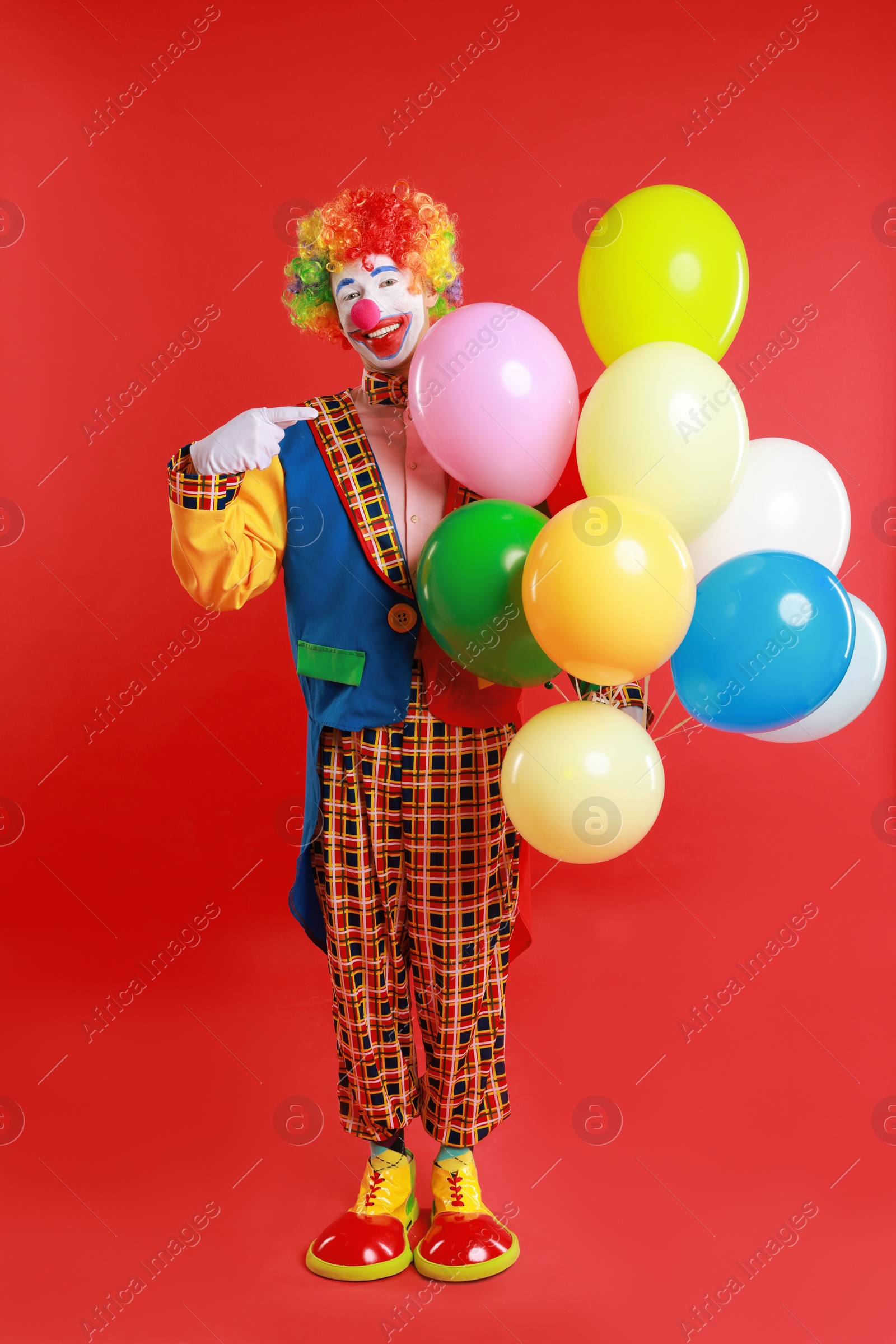 Photo of Happy clown with colorful balloons on red background