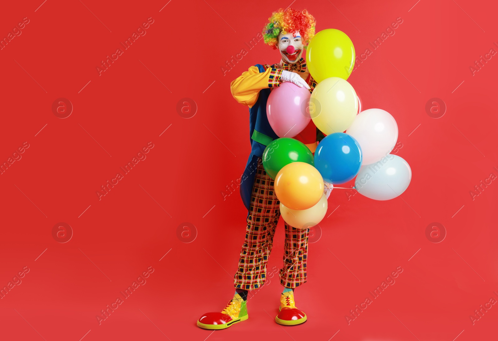 Photo of Happy clown with colorful balloons on red background