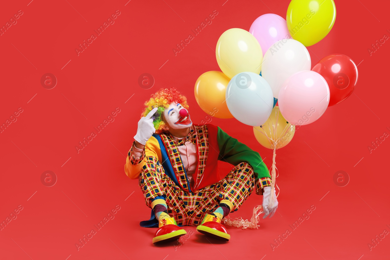 Photo of Happy clown with colorful balloons on red background